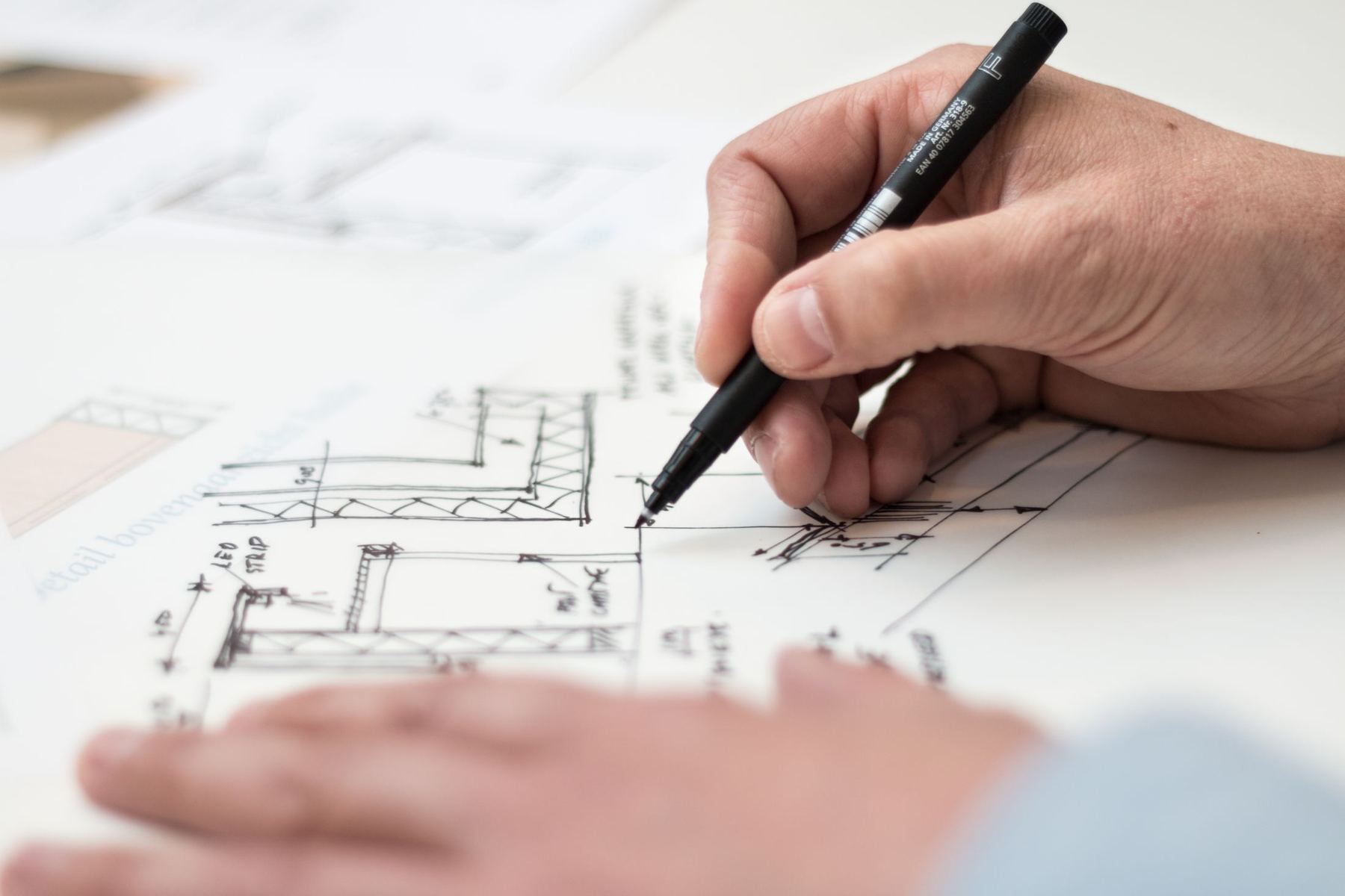 A hand marking up architectural drawings with a pen