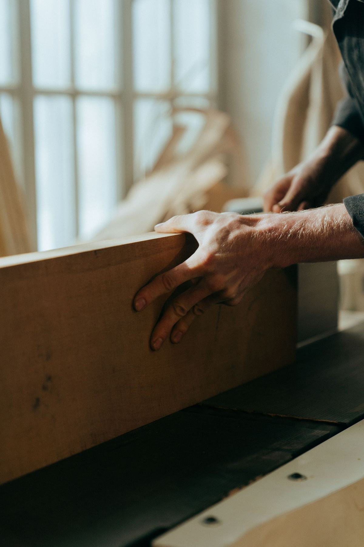 A pair of hands steadying a length of planed timber on a bench